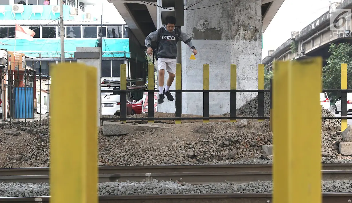 Seorang siswa melompati pagar perlintasan kereta api di kawasan Tanjung Barat, Jakarta, Senin (7/1). Sejumlah pejalan kaki tetap memilih untuk melompati pagar pembatas dari pada menggunakan fasilitas JPO. (Liputan6.com/Immanuel Antonius)