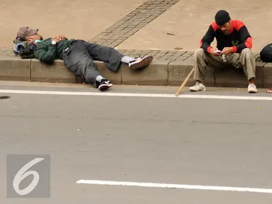 Massa aksi damai beristirahat di pinggir Jalan Merdeka Barat jelang bergerak menuju Istana Negara, Jakarta, Jumat (4/11). Massa melakukan aksi di depan Istana Negara menuntut penegakan hukum kasus dugaan penistaan agama. (Liputan6.com/Helmi Fithriansyah)