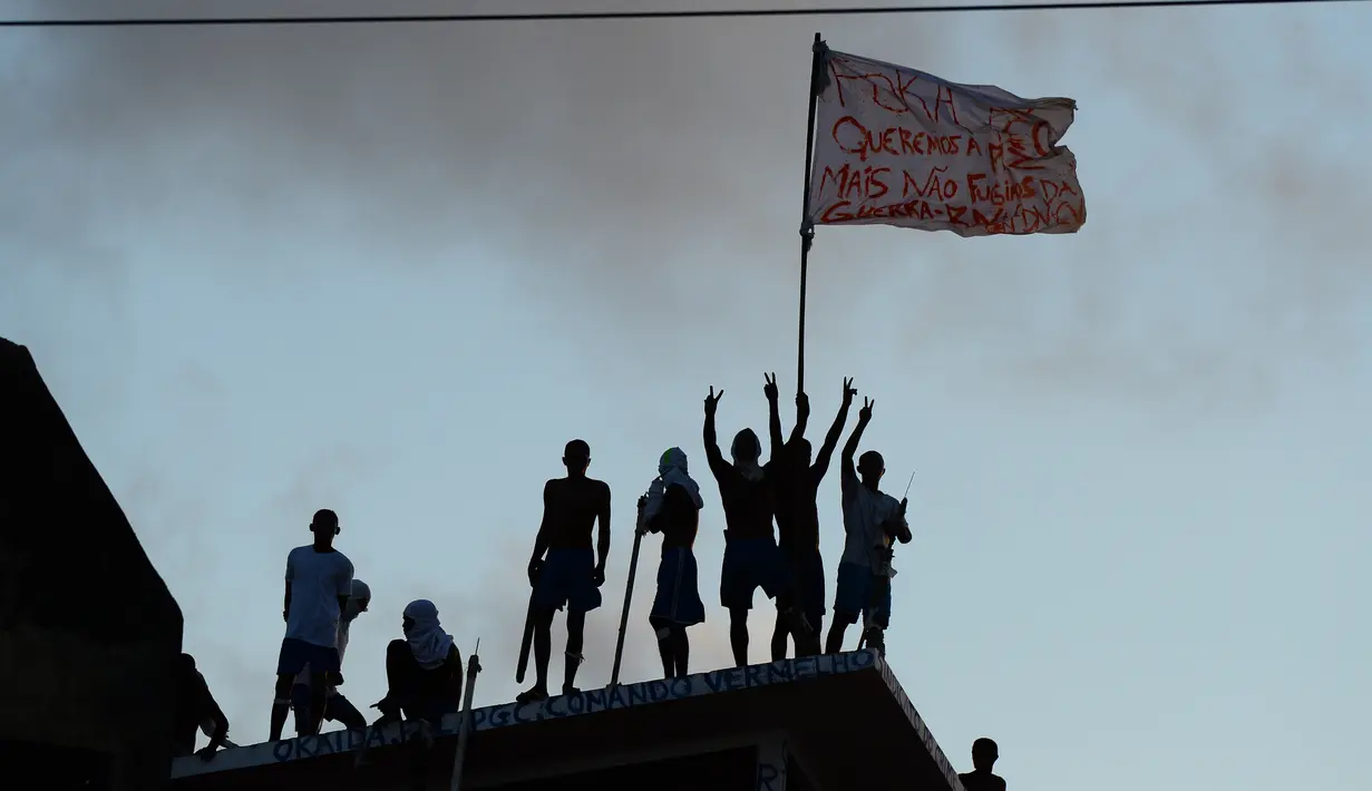 Para tahanan mengibarkan bendera diatas atap usai bentrokan antar dua geng narkoba di penjara Alcacuz, Rio Grande do Norte, Brasil, (16/1). Sebagian besar jenazah ditemukan dalam kondisi termutilasi. (AFP Photo/Andressa Anholette)