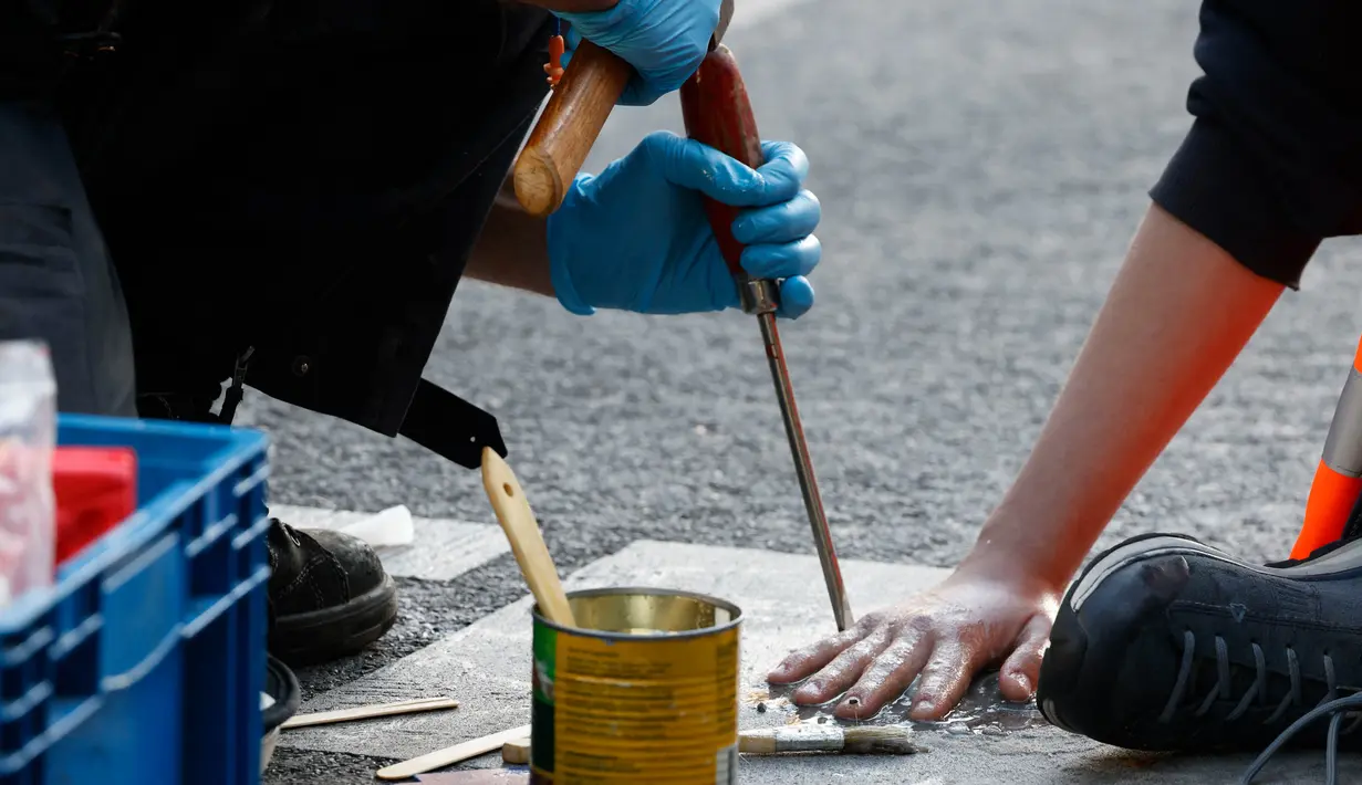 Seorang polisi menggunakan alat untuk menyingkirkan seorang aktivis iklim yang menempelkan dirinya di jalan untuk menarik perhatian pada aksi keadaan darurat iklim gerakan Letzte Generation (Generasi Terakhir), pada 18 September 2023 di Berlin. (Odd ANDERSEN/AFP)