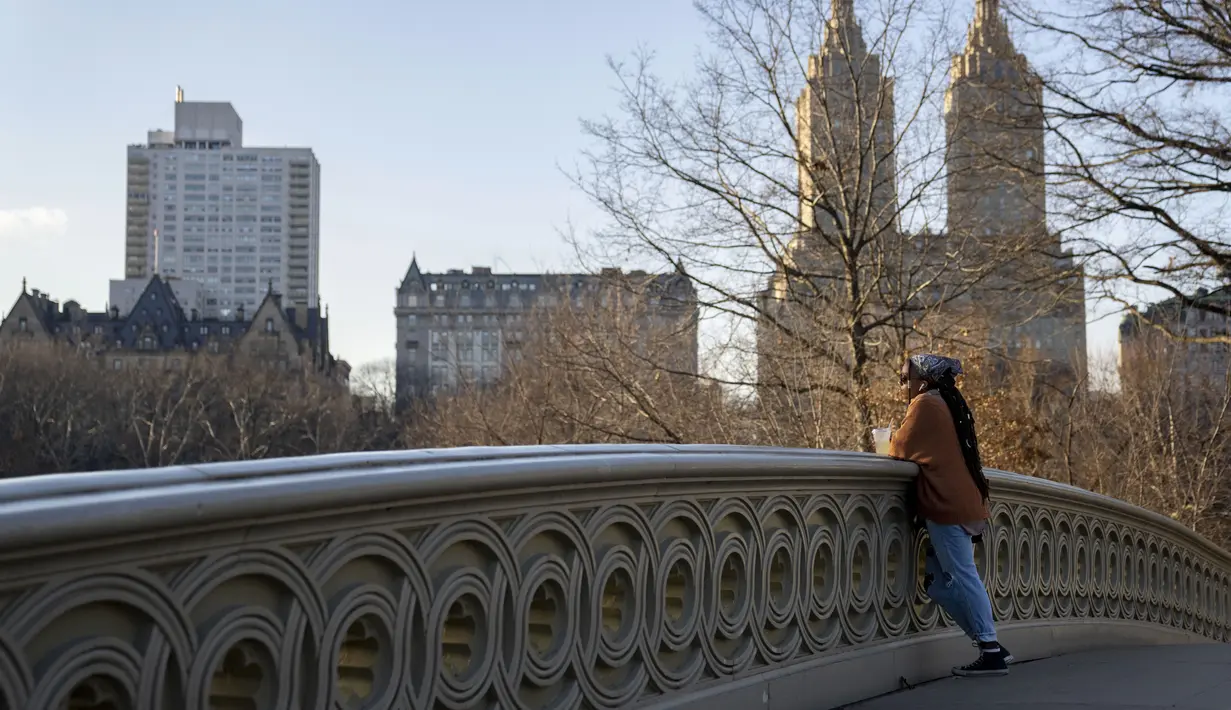 Seorang pengunjung berjemur di bawah sinar matahari di Bow Bridge di Central Park, wilayah Manhattan, New York, Senin (30/1/2023). Terakhir kali butuh waktu lama sebelum salju bertahan di tanah pada musim dingin adalah tahun 1973, ketika warga New York harus menunggu hingga 29 Januari. (AP Photo/John Minchillo)