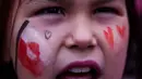 Bendera merah-putih Greenland berkibar di antara sejumlah poster penolakan. Tampak dalam foto, seorang gadis berteriak saat protes menentang kebijakan Presiden Amerika Serikat (AS), Donald Trump, terhadap Greenland di depan konsulat AS di Nuuk, Sabtu 17 Januari 2026. (AP Photo/Evgeniy Maloletka)