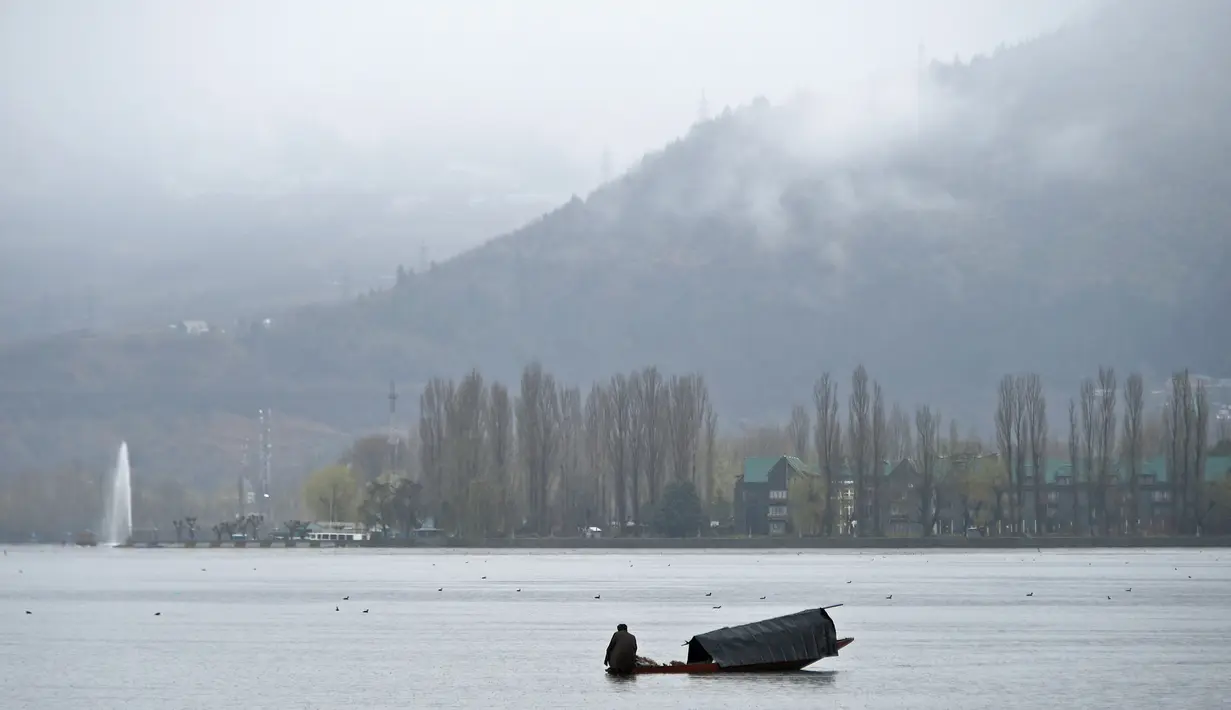 Seorang awak perahu Kashmir mengayuh sebuah perahu saat hujan di Danau Dal di Srinagar (20/3). Danau Dal dijuluki sebagai Jewel in the Crown of Kashmir atau Srinagar Jewel. (AFP Photo/Tauseef Mustafa)
