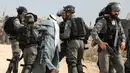 Pasukan penjaga perbatasan Israel menahan seorang pria Palestina di tengah-tengah bentrokan dengan para pengunjuk rasa yang berdemonstrasi menentang pembangunan pos terdepan Israel di dekat desa Palestina, Ramallah, Tepi Barat, Kamis (17/10/2019). (Jaafar ASHTIYEH/AFP)