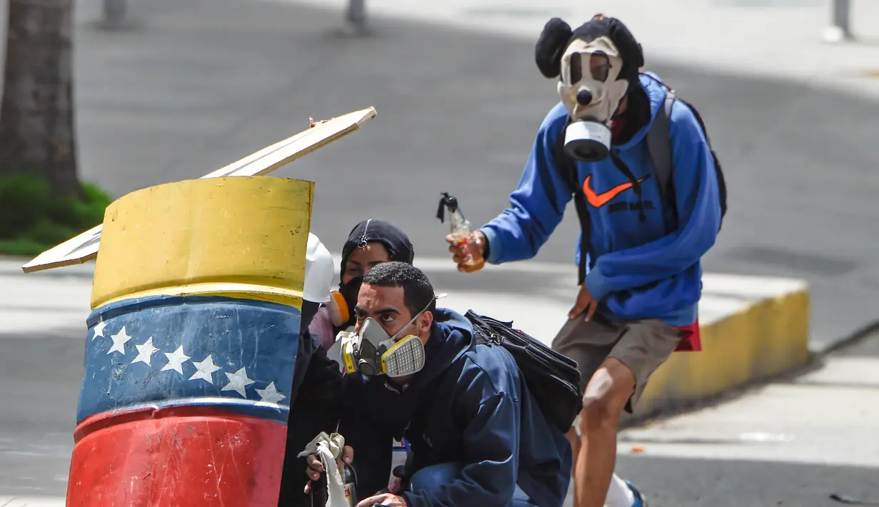 Pengunjuk rasa berada di balik tameng saat mereka bentrok dengan polisi antihuru-hara menuntut Presiden Venezuela, Nicolas Maduro, di Caracas (10/7). Salah satu demonstran mengenakan pelindung wajah karakter Mickey Mouse. (AFP Photo/Juan Barreto)