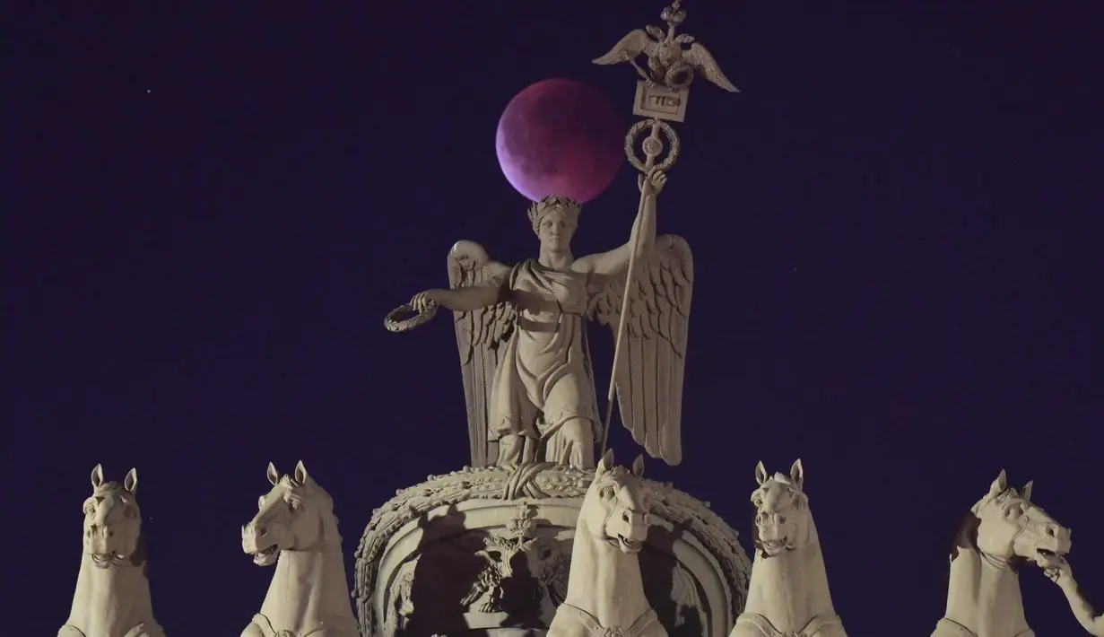 Fenomena langit langka, gerhana bulan total, kembali menghiasi langit di berbagai belahan dunia pada Minggu malam hingga Senin dini hari, 7-8 September 2025. Tampak dalam foto, fase gerhana bulan total terlihat di belakang Kereta Triumphal di puncak Gerbang Staf Umum di Saint Petersburg, Rusia pada 7 September 2025. (Olga MALTSEVA/AFP)