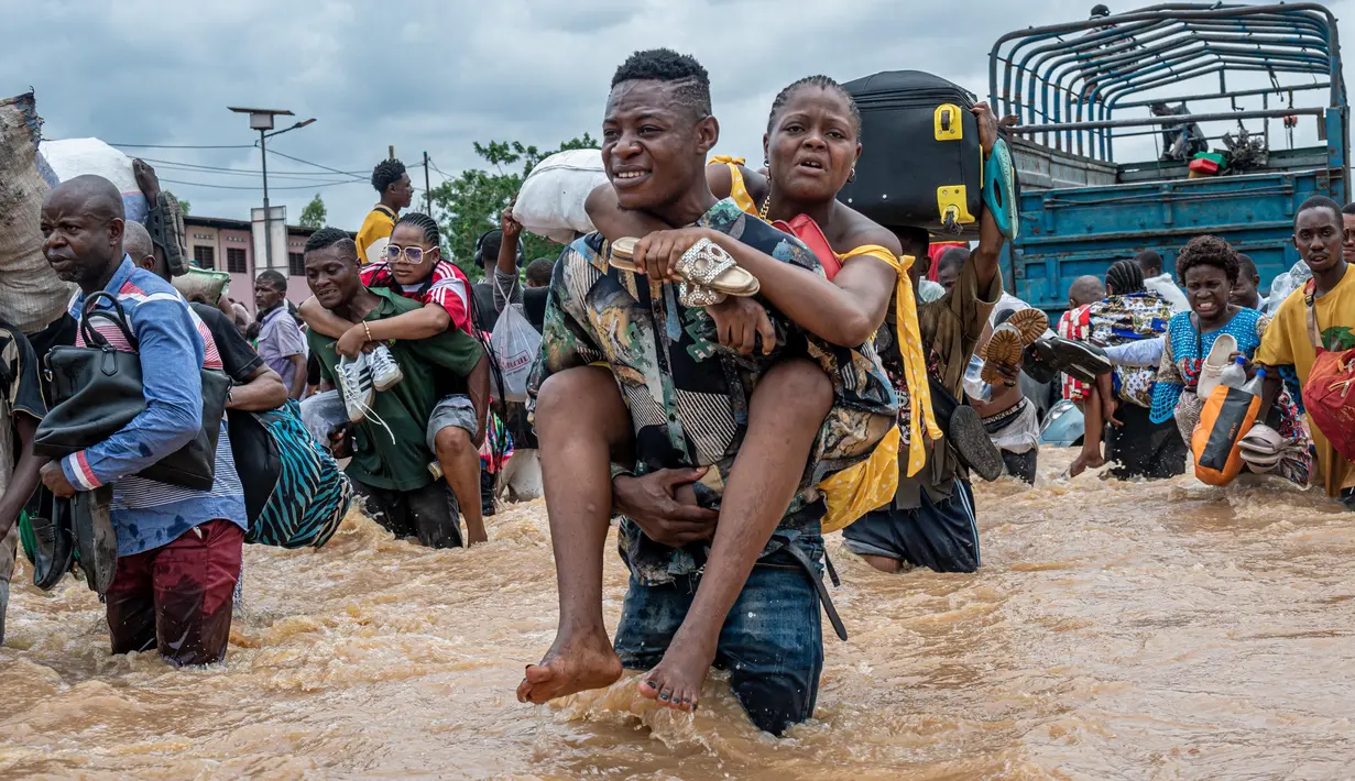 Warga menggendong seorang perempuan sementara lainnya menyeberangi banjir di distrik Ndjili, Kinshasa, pada 6 April 2025. (Hardy BOPE/AFP)