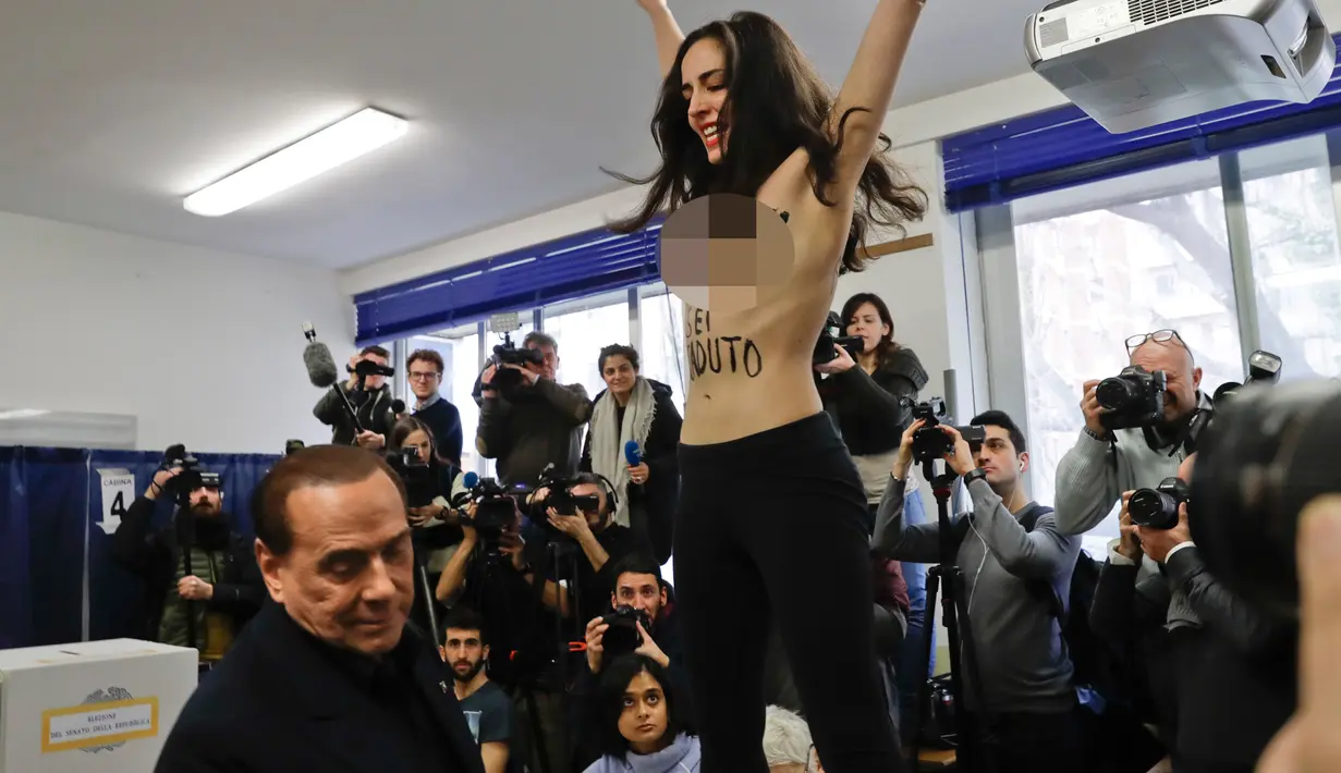 Seorang aktivis Femen bertelanjang dada di depan mantan PM Italia dan pemimpin partai Forza Italia Silvio Berlusconi di Milan, Italia, Minggu (4/3). Lebih dari 46 juta orang Italia memilih pada hari ini. (AP Photo/Luca Bruno)