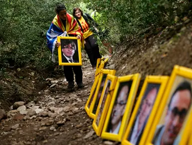 Seorang wanita memegang foto presiden terguling Catalonia, Carles Puigdemont saat mereka menjejerkan potret orang-orang yang dipenjara dan diasingkan di Gunung Montserrat, Spanyol (28/4). (AFP/Pau Barrena)