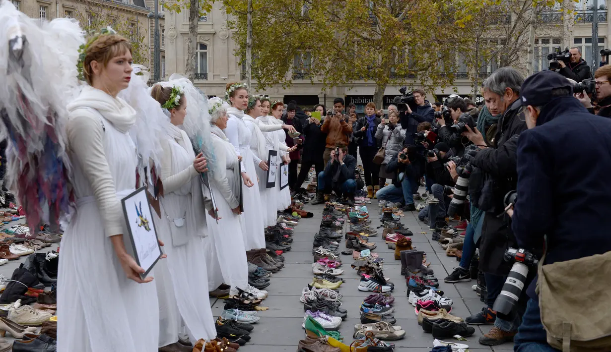 Perempuan berpakaian seperti malaikat berdiri di antara sepatu yang dipajang di place de la Republique, Prancis, sebagai tanda solidaritas karena pawai lingkungan di Paris dibatalkan jelang KTT Perubahan Iklim, Minggu (29/11).(AFP PHOTO/Miguel Medina)