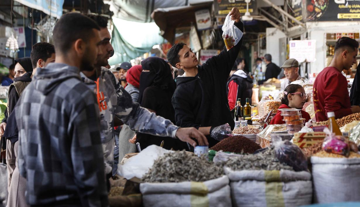 Warga Palestina di Kota Gaza tetap berupaya menghidupkan nuansa khas menyambut bulan suci Ramadan 1447 Hijriah. Tampak dalam foto, warga Palestina berbelanja buah-buahan kering dan kacang-kacangan di pasar Zawiya, Kota Gaza, pada Rabu 18 Februari 2026. (Omar AL-QATTAA/AFP)