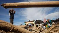 Selain rumah warga terdampak, kayu-kayu gelondongan juga masih terlihat tertumpuk di sepanjang aliran Sungai Aek Garoga dan Sungai Batang Toru. Tampak dalam foto, para penyintas berjalan melewati tumpukan kayu yang tersapu banjir bandang di Batang Toru, Sumatra Utara, Selasa 2 Desember 2025. (AP Photo/Binsar Bakkara)