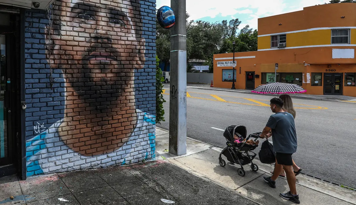 Pejalan kaki melintasi mural wajah Lionel Messi yang berada di salah satu jalan di Miami, Amerika Serikat. Messi memutuskan untuk bergabung dengan klub MLS, Inter Miami, pada Rabu (7/6/2023). (AFP/Giorgio Viera)