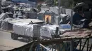 Truk-truk yang mengangkut bantuan yang masuk ke Jalur Gaza melalui pos perbatasan Karm Abu Salem, melintas di dekat tenda-tenda pengungsian di kamp pengungsi Nuseirat di bagian tengah Jalur Gaza, pada Selasa 14 Oktober 2025. (Eyad BABA/AFP)