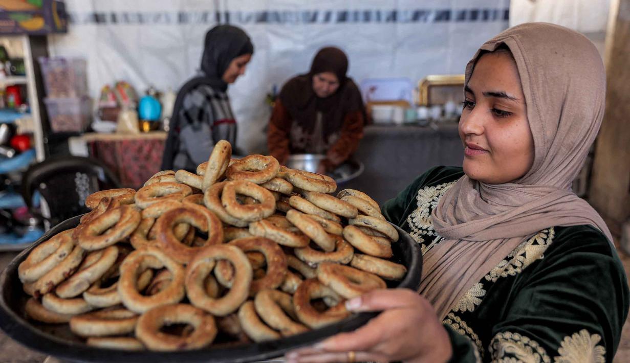 Kue ini sering dianggap sebagai camilan khas. Tampak dalam foto, seorang wanita memegang nampan berisi biskuit tradisional "kaak" yang berbentuk cincin dan baru dipanggang menjelang Idul Fitri, hari raya yang menandai berakhirnya bulan puasa suci Ramadhan, di Kota Gaza pada 16 Maret 2026. (Omar AL-QATTAA/AFP)