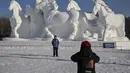 Seorang pria berpose di depan patung salju raksasa di Pameran Seni Patung Salju Internasional Harbin Sun Island menjelang Festival Es dan Salju Internasional Harbin Tiongkok ke-39 di Harbin, di provinsi Heilongjiang timur laut China (4/1/2023). (AFP/Hector Retamal)
