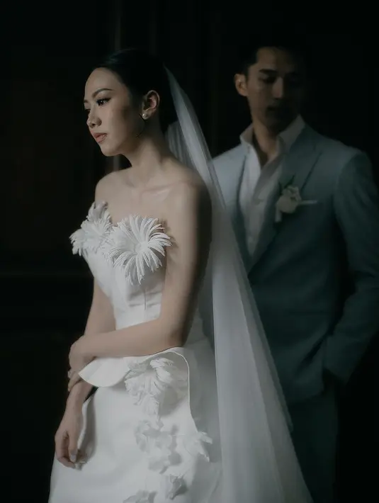 Shanju mengenakan gaun pernikahan strapless yang memiliki aksen bunga-bunga putih di bagian dada. Sementara itu, Jonatan tampil gagah dengan setelan jas abu-abu. [@elsiechrysila]