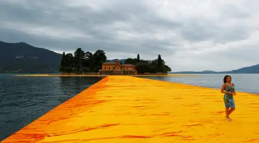 Seorang wanita berjalan diatas instalasi seni 'The Floating Piers' buatan seniman kelahiran Bulgaria Christo Vladimirov Yavachev atau dikenal sebagai Christo , di Danau Iseo , Italia utara , (16/6). (REUTERS / Stefano Rellandini)