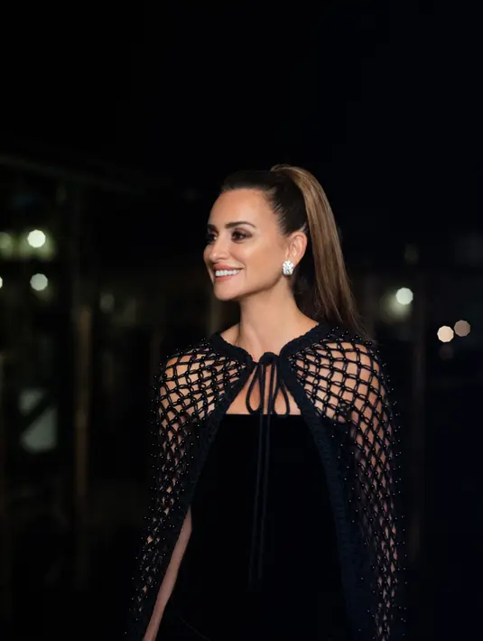 Penelope Cruz memakai bustier velvet dress hitam dengan cape beretail pearls