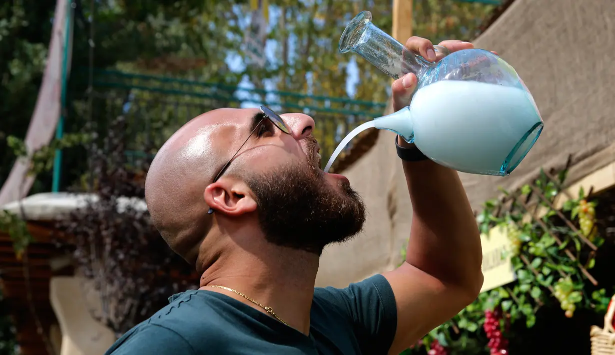 Seorang pria meminum arak dari kendi kaca tradisional selama perayaan minuman beralkohol Lebanon di Kota Taanayel, 8 September 2018. Arak khas Lebanon tersebut berwarna putih susu. (AP Photo/Hussein Malla)