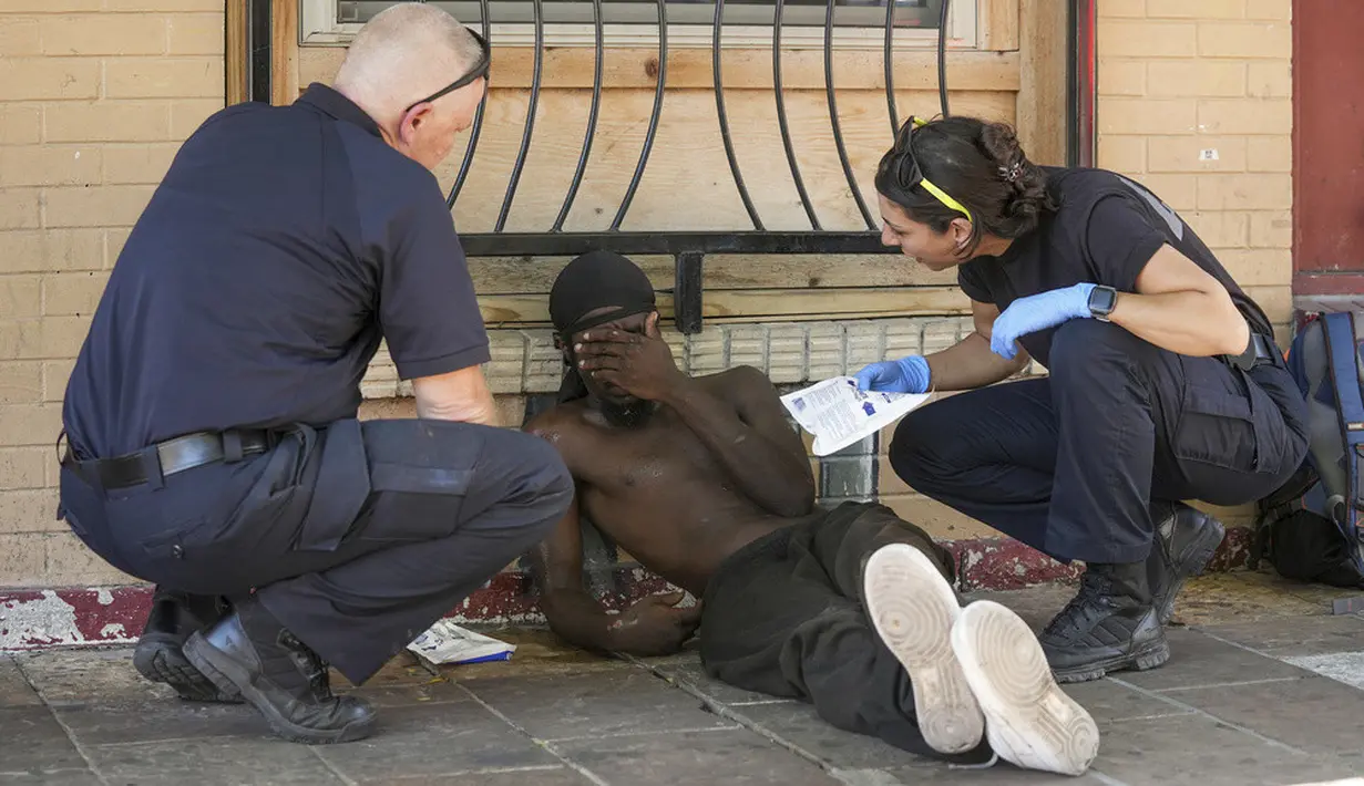<p>Petugas Layanan Medis Darurat Austin-Travis Kapten Darren Noak (kiri) dan M. Megally memeriksa seorang pria saat peringatan panas berlebihan ketika suhu mencapai 107 derajat di East 6th Street di Austin, Texas, Amerika Serikat, 12 Juli 2023. Pria itu kemudian diangkut menggunakan ambulans ke rumah sakit karena masalah terkait panas. (Jay Janner/Austin American-Statesman via AP)</p>