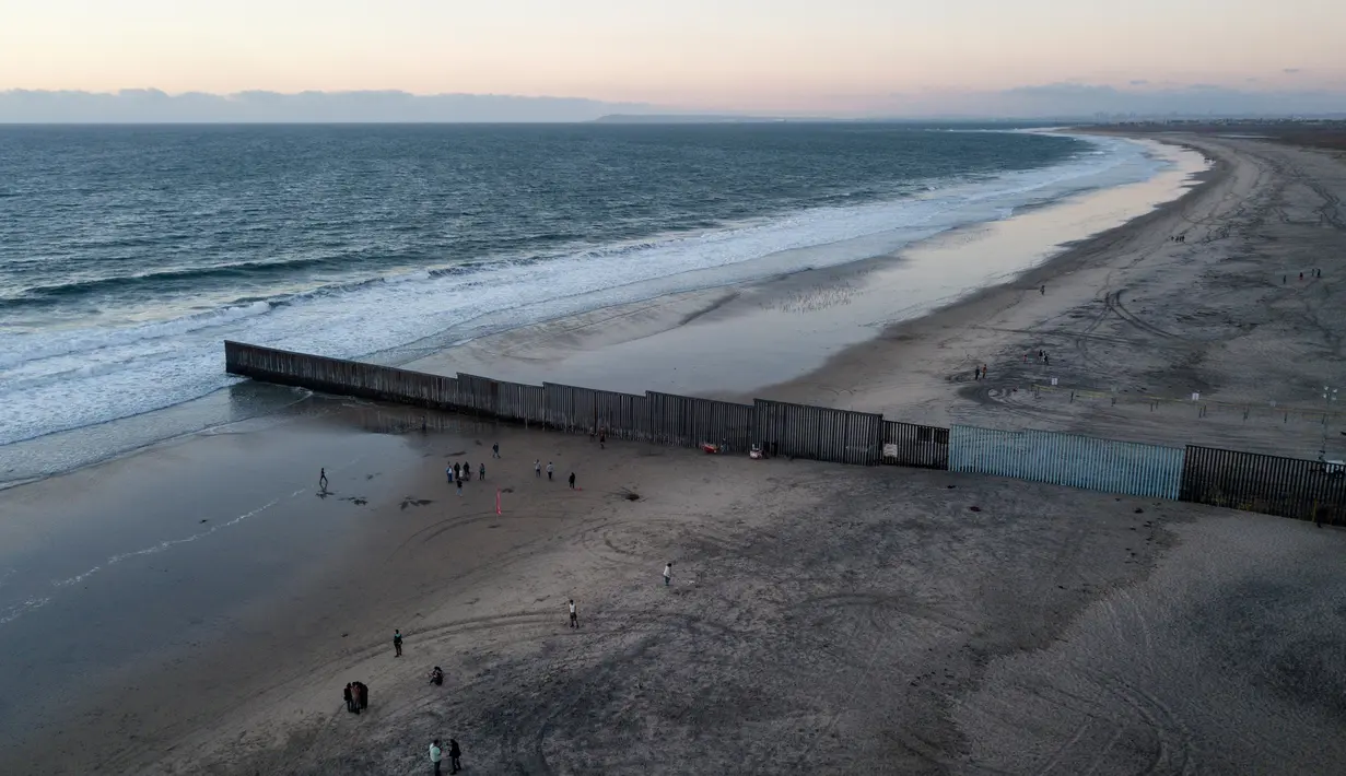 Orang-orang berjalan di pantai dekat perbatasan AS dan Meksiko di Tijuana, Meksiko, Jumat (23/11). Selama beberapa pekan terakhir pemerintahan AS telah berusaha menahan laju rombongan imigran masuk ke negaranya. (AP Photo/Rodrigo Abd)