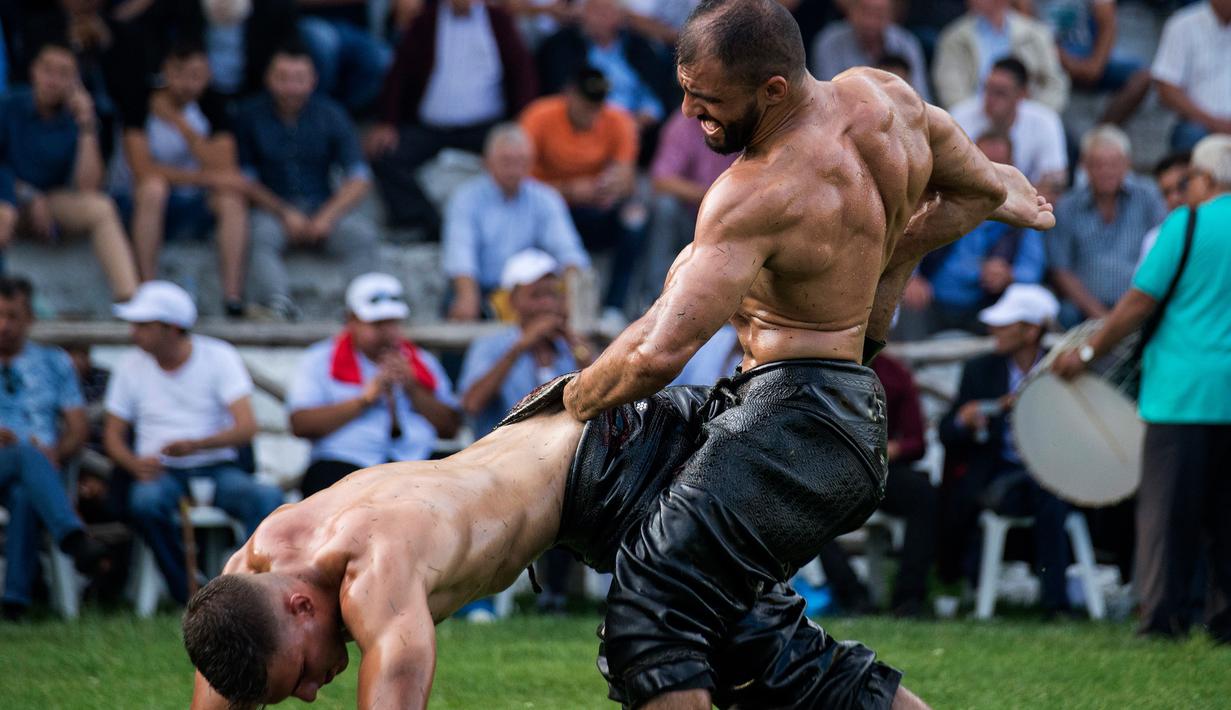 Pegulat menggenggam celana lawan sebelum membantingnya dalam kompetisi tahunan gulat minyak tradisional di Sochos, Yunani, 30 Juni 2018. Pertandingan perpaduan tradisi Yunani kuno dan zaman modern itu diiringi musik tradisional. (AP/Giannis Papanikos)