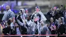 Meskipun hujan deras, semangat para atlet tetap tinggi untuk terus mengikuti upacara pembukaan dengan mengenakan jas hujan bening yang menutupi busana parade mereka.  (AP Photo/Kirsty Wigglesworth)