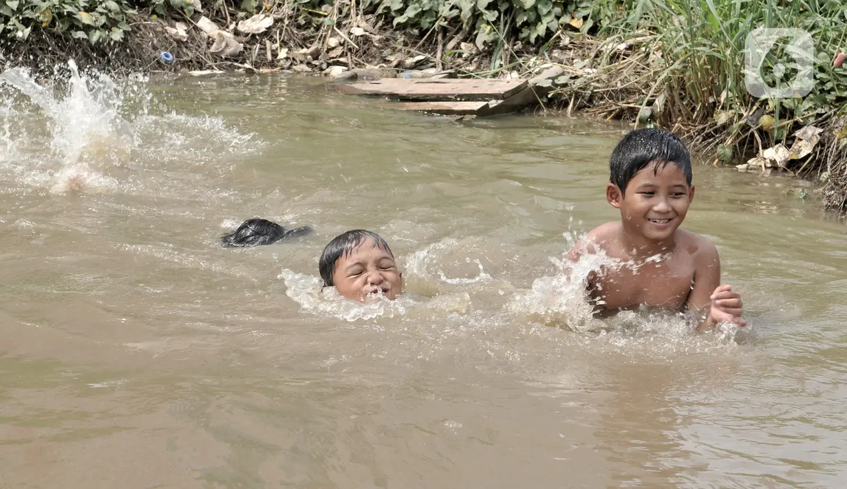 Anak-anak berenang di kubangan air di depan Apartemen Green Pramuka, Jakarta, Rabu (5/2/2020). Keterbatasan ekonomi dan minimnya lahan bermain membuat sekelompok anak sekolah dasar ini memilih berenang di kubangan meskipun mereka tahu air kotor dapat menimbulkan penyakit. (merdeka.com/Iqbal Nugroho)