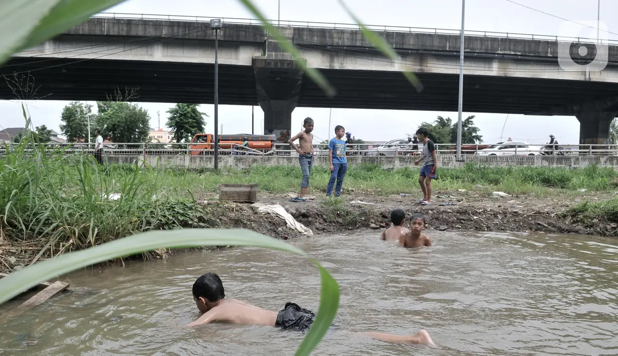 Anak-anak berenang di kubangan air di depan Apartemen Green Pramuka, Jakarta, Rabu (5/2/2020). Keterbatasan ekonomi dan minimnya lahan bermain membuat sekelompok anak sekolah dasar ini memilih berenang di kubangan meskipun mereka tahu air kotor dapat menimbulkan penyakit. (merdeka.com/Iqbal Nugroho)