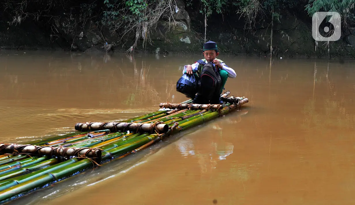 Seorang anak menyeberangi Sungai Cikaniki dengan rakit di Rumpin, Bogor, Jawa Barat, Rabu (15/1/2020). Akibat banjir bandang merobohkan jembatan yang menghubungkan Desa Tonjong Rumpin dan Desa Kantalarang Leuwiliang, warga terpaksa memanfaatkan perahu rakit untuk melintas. (merdeka.com/Arie Basuki)