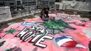 Seniman berusia 16 tahun, S.F. melukis mural tentang pandemi virus corona COVID-19 di atap gedung di Athena, Yunani, Senin (23/3/2020). (Aris Messinis/AFP)