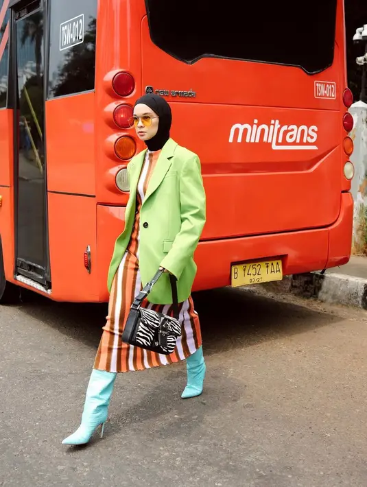 Kunci untuk terlihat bold saat mengenakan outfit yang semarak adalah percaya diri. Kerennya Tantri Namirah saat memadukan dress bercorak garis-garis vertical bernuansa oranye-kecokelatan, dengan oversized blazer hijau, dan high boots biru mint, serta tas tangan hitam bercorak zebra. [Foto: Instagram/tantrinamirah]