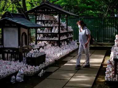 Pengunjung yang mengenakan masker berjalan melewati patung-patung maneki-neko di Kuil Gotokuji, Tokyo, Jepang, Rabu (10/6/2020). Kuil Gotokuji terkenal karena dipercaya sebagai tempat kelahiran maneki-neko, kucing pembawa keberuntungan. (Philip FONG/AFP)