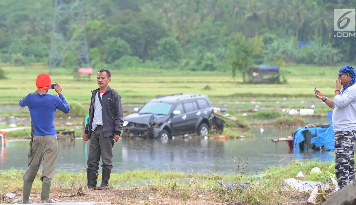 Warga berselfie dengan latar belakang kawasan terdampak bencana tsunami di Carita, Banten, Selasa (25/12). Libur Natal dimanfaatkan warga luar Anyer dan carita untuk menyaksikan langsung terdampak bencana sambil berselfie. (Merdeka.com/Arie Basuki)