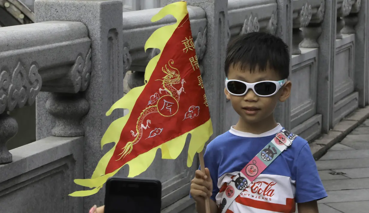 Seorang anak memegang bendera untuk difoto saat mengikuti lomba perahu naga di kawasan bersejarah Teluk Lychee di Guangzhou, Provinsi Guangdong, China selatan, Jumat, 3 Juni 2022. Perlombaan perahu naga kembali digelar di beberapa bagian China untuk pertama kalinya sejak merebaknya pandemi pada akhir 2019, saat pembatasan dicabut bersama dengan penurunan besar  kasus COVID-19. (AP Photo/Caroline Chen)