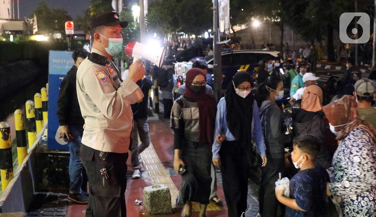 Polisi melakukan imbauan menggunakan pengeras suara terhadap warga yang berkerumun di kawasan Bundaran HI, Jakarta, Jumat (31/12/2021). Untuk mencegah penyebaran COVID-19, petugas gabungan melakukan pembubaran aktivitas warga di malam Tahun Baru. (Liputan6.com/Angga Yuniar)