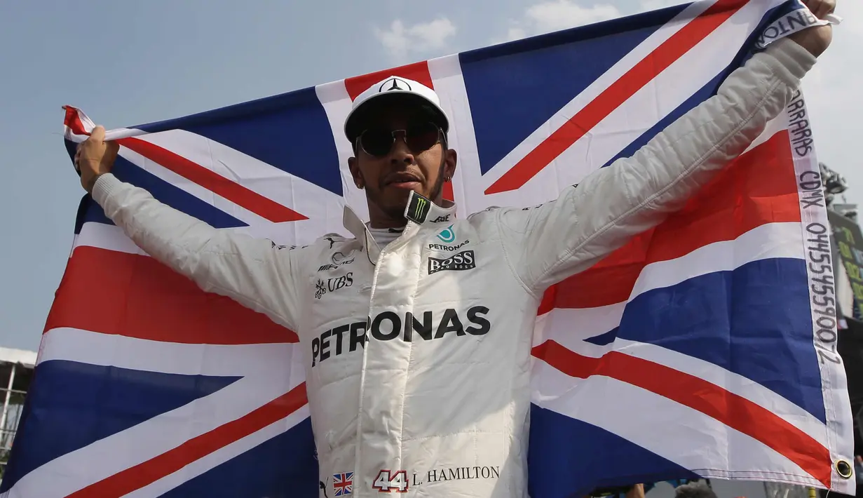 Lewis Hamilton membentangkan bendera negaranya saat merayakan kemenangannya meraih juara dunia F1 untuk yang ke empat kalinya di Autodromo Hermanos Rodrigue, Meksiko (29/10). (AP Photo / Moises Castillo)