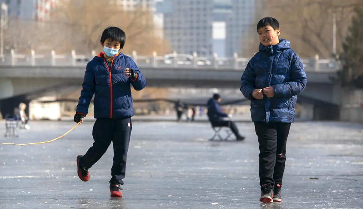 Seorang anak laki-laki yang memakai masker wajah untuk melindungi dari penyebaran virus corona COVID-19 berjalan melintasi permukaan kanal yang membeku di Beijing, China, Sabtu (30/1/2021). (AP Photo/Mark Schiefelbein)