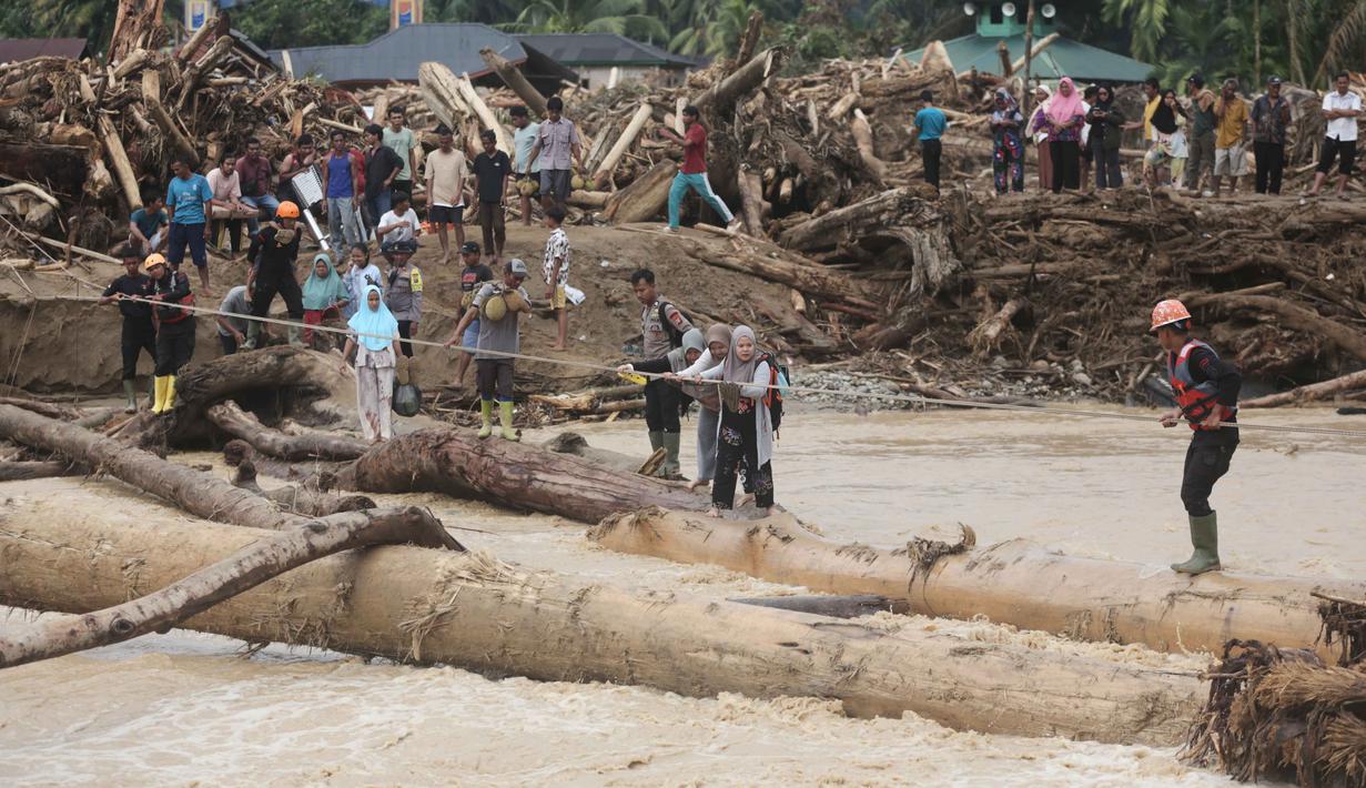 Warga yang menjadi korban banjir bandang di Batang Toru, Tapanuli Selatan, Sumatra Utara menggunakan kayu gelondongan untuk menyeberangi sungai, Selasa 2 Desember 2025. Warga Batang Toru, Tapanuli Selatan, terpaksa menggunakan jembatan darurat yang terbuat dari gelondongan kayu untuk menyeberangi sungai setelah jembatan utama rusak akibat terjangan banjir bandang baru-baru ini. (AP Photo/Binsar Bakkara)