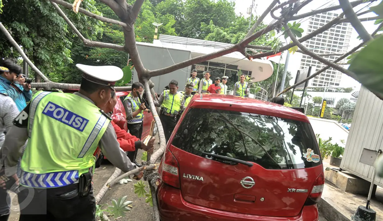 Petugas dibantu warga memindahkan pohon tumbang yang menimpa mobil saat terparkir di sebelah Pos Polisi Bundaran HI, Jakarta, Selasa (15/12). Tak ada korban jiwa akibat tumbangnya pohon yang disebabkan angin kencang tersebut. (Liputan6.com/Faizal Fanani)