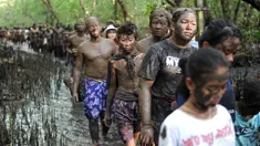 Warga Bali berjalan bersama dengan badan penuh lumpur saat mengikuti mandi lumpur tradisional atau yang dikenal sebagai Mebuug-buugan di desa Kedonganan, Bali (18/3). (AFP/Sony Tumbelaka)