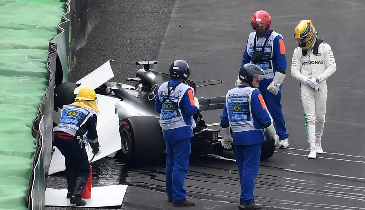 Pembalap Mercedes, Lewis Hamilton (kanan) melihat mobilnya usai menabrak saat kualifikasi F1 GP Brasil di sirkuit Interlagos di Sao Paulo, Brasil (11/11). Mobil Hamilton itu hancur sehingga bendera merah harus berkibar. (AFP Photo/Nelson Almeida)