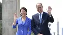 Pangeran William dan Kate Middleton melambaikan tangan sambil berpose di depan Gerbang Brandenburg di Berlin, Rabu (19/7). Pangeran William terlihat mengenakan setelan biru navy model klasik dan dasi biru untuk mengimbangi sang istri (John MACDOUGALL/AFP)