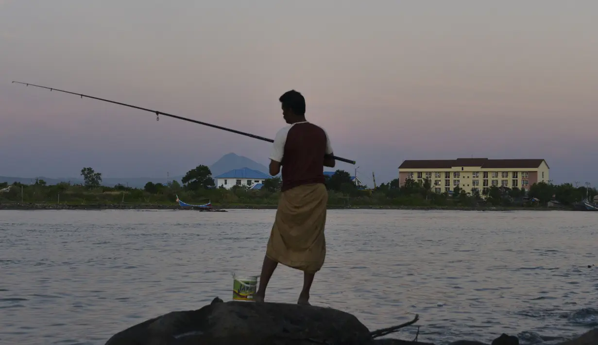Seorang pria memancing saat matahari terbenam atau sunset di Banda Aceh pada 28 Juni 2019. Suasana eksotis menuju temaram bisa dinikmati sembari berjalan menyusuri pantai di tengah cahaya matahari yang mulai memerah. (Photo by CHAIDEER MAHYUDDIN / AFP)