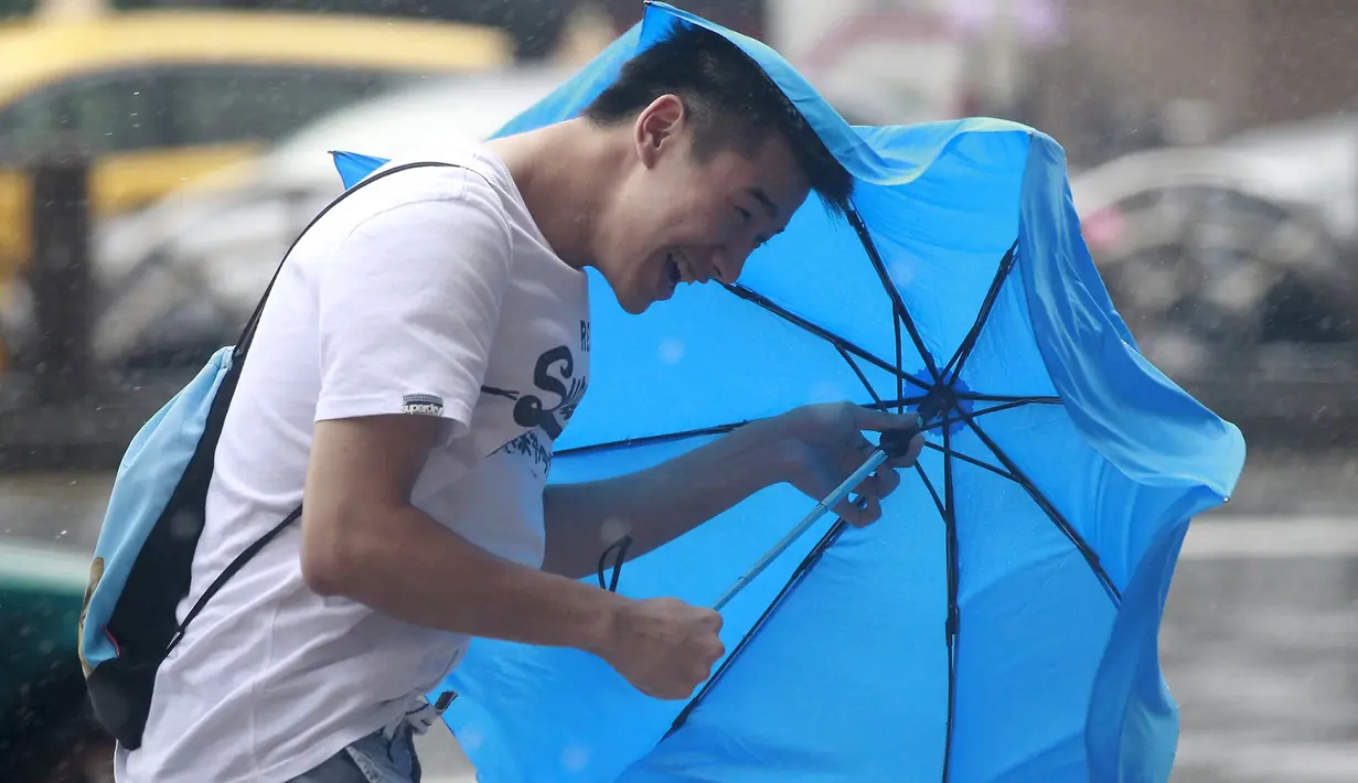 Seorang pria memegang payung sambil berjalan menghindari angin kencang yang disebabkan topan Dujuan di Taipei, Taiwan, Senin (28/9). Ribuan orang diungsikan untuk menghadapi topan Dujuan yang diprediksikan akan menyerang Taiwan. (REUTERS/Pichi Chuang)