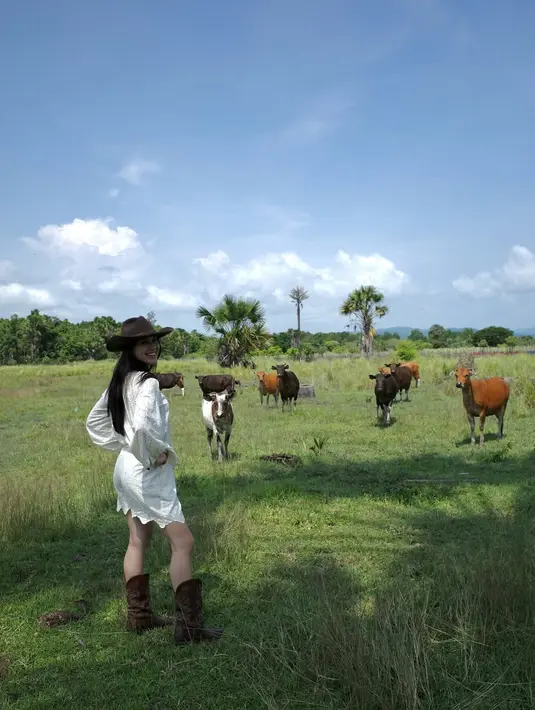 Tak hanya berinteraksi dengan kuda, Yasmin juga mencoba menggembalakan sapi seperti layaknya seorang koboi. Dengan sepatu bot dan senyuman lebar, ia berdiri penuh gaya sambil memandang kamera. Kehadiran sapi-sapi yang merumput di latar belakang semakin melengkapi suasana otentik ala koboi yang ia jalani.  (Liputan6.com/IG/@yasminnapper)
