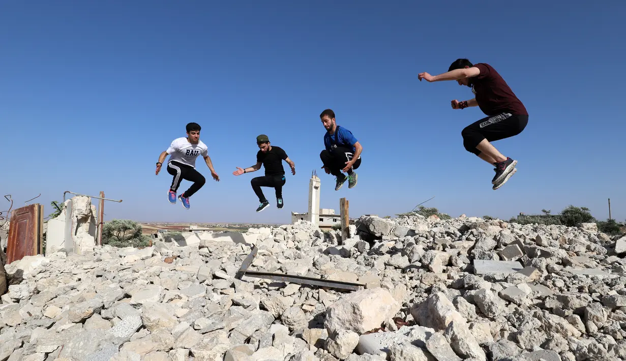 Pemuda Suriah melakukan olahraga ekstrem parkour di atas reruntuhan bangunan yang hancur akibat serangan pasukan rezim di kota Binnish di provinsi barat laut Idlib pada 17 Juni 2020. Parkour merupakan olahraga ketangkasan yang terdiri dari lari, melompat, salto dan berayun. (Abdulaziz KETAZ / AFP)