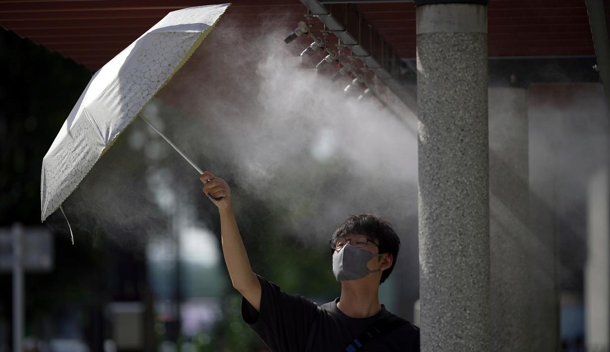 Seorang pria yang mengenakan masker wajah untuk membantu melindungi dari penyebaran virus corona mendinginkan diri di titik kabut yang menyejukkan, Tokyo, Jepang, 1 Agustus 2022. Cuaca panas terus berlanjut di wilayah metropolitan karena suhu diperkirakan akan meningkat hingga 35 derajat Celcius (95 derajat Fahrenheit), menurut biro meteorologi Jepang. (AP Photo/Eugene Hoshiko)