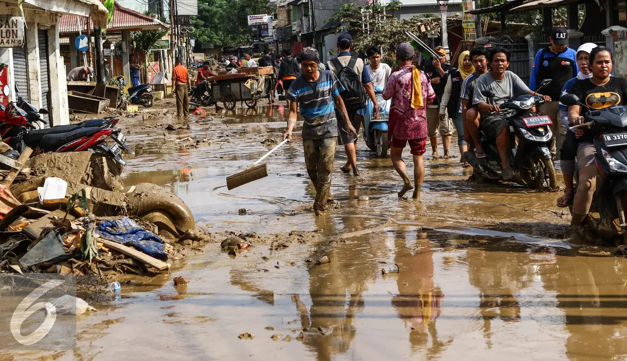 Warga dan pengendara motor melintas di sepanjang jalan yang dipenuhi lumpur di komplek Pondok Gede Permai Jatiasih, Bekasi, Jumat (22/04).Banjir yang telah merendam ratusan rumah warga mengakibatkan air lumpur mengendap. (Liputan6.com/Fery Pradolo)